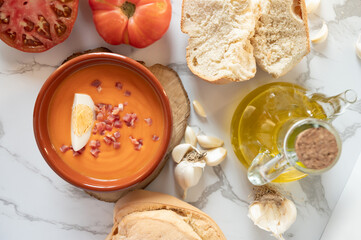 Spanish salmorejo with tomatoes, garlic, bread and olive oil decorating a marble table