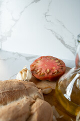 Simple composition with mediterranean diet ingredients such as bread, tomato, garlic and olive oil, lying on a wooden cutting board