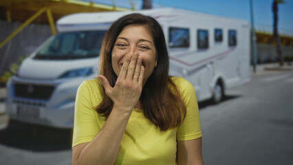Middle age woman in yellow shirt covers mouth with finger to lips gesture on sunlit urban street by...