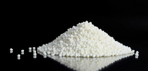 A mound of white polypropylene pellets sits on a reflective surface against a black backdrop,  black background,  plastic granules