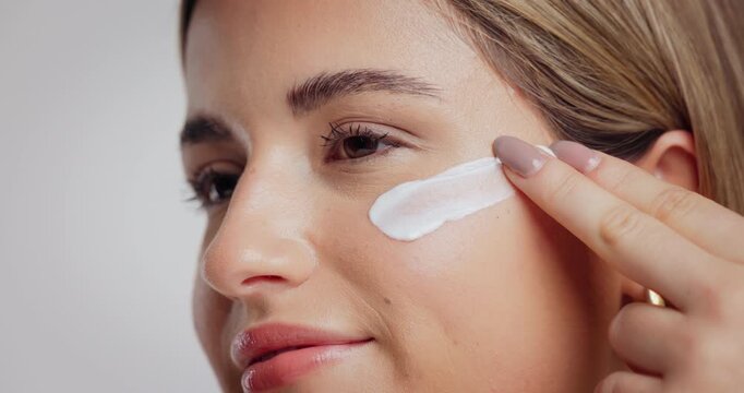 Beauty, woman and apply face cream in studio for hydration treatment, moisturizer or hyaluronic acid. Skincare, person and SPF lotion on white background for healthy skin, self care routine and glow