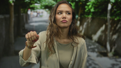 Woman expressing emotion outdoors with lush trees in the background, wearing a beige coat and watch, conveying a sense of contemplation and thoughtfulness.