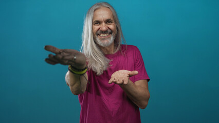 Man with palms up presenting open hands in a teal studio, long silver hair, bracelets and casual tshirt visible; openness joy.