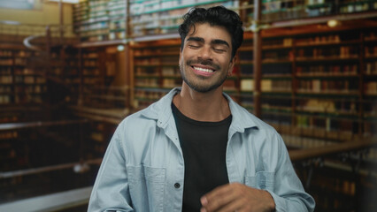 Man tilts head back with hand to mouth while laughing in a historic library with wooden bookshelves...