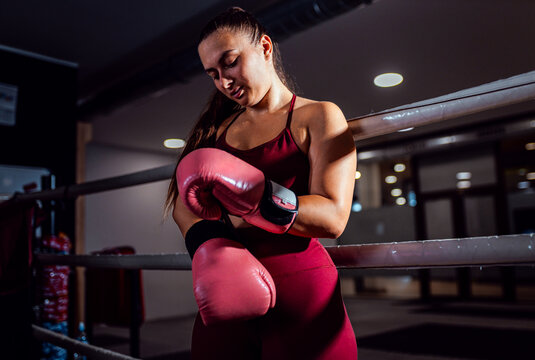 Confident female boxer putting gloves on hands preparing for training in boxing ring.