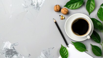 Coffee, pencil, walnuts, paper and foliage lay atop a gray textured surface. The setting is bright, airy and modern