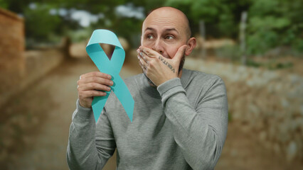 Man with beard holding blue ribbon outdoors expressing surprise in a park setting, symbolizing...
