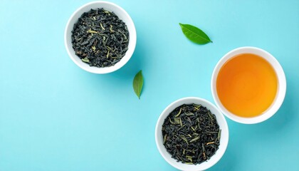 Top-down view two bowls of tea leaves, one bowl of brewed tea, and green leaves on a light blue background