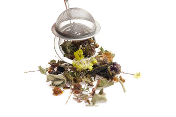 Herbal tea ingredients spilling from a metal strainer onto a white surface, showcasing vibrant...