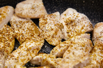 Fresh chicken fillets seasoned with spices are sizzling in a frying pan, showcasing a delicious...