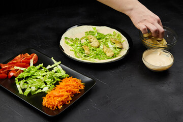 Fresh ingredients being prepared for a healthy wrap, featuring lettuce, tomatoes, and carrots, with a hand adding sauce, showcasing vibrant colors and culinary creativity