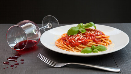Delicious spaghetti with tomato sauce and a glass of spilled wine