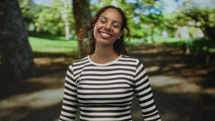 Woman smiling with visible face and tilted head, wearing striped top and gold necklace, standing on...