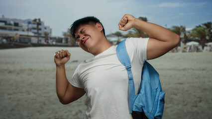 Young chinese man stretching at seaside, wearing white shirt and blue backpack, enjoying outdoor beach setting, capturing student relaxation and serene sea view.