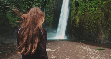 Young woman with long brown hair is enjoying a beautiful waterfall in a tropical jungle forest. The...
