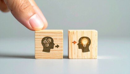 Hand gently places two wooden blocks displaying a head icon with gears and a head icon with a lightbulb, on a neutral background, conveying idea transmission