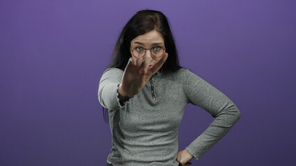 Woman with glasses and brunette hair gesturing no with her finger against a vibrant purple...