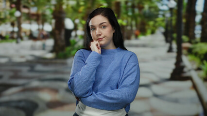 Woman in blue sweater contemplating on a beautiful street with lush green foliage outdoors during a sunny day in an urban area, showcasing a serene atmosphere.