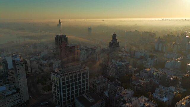 Drone view of sunrise in Montevideo, Uruguay, covered by fog. Buildings emerge faintly from the fog