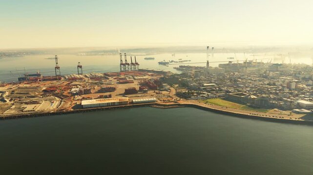 view of the Port of Montevideo with cranes, and ships in the distance under a hazy sky at sunset