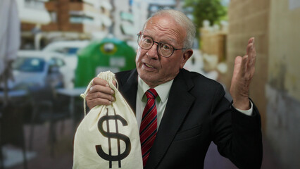 Senior man in business suit holding a dollar-marked bag on an outdoor terrace in a restaurant...