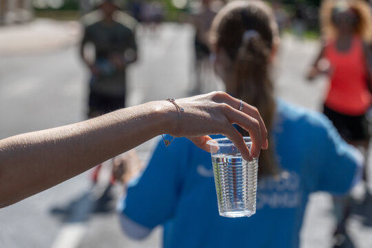A close-up of a volunteer's hand offering a cup of water to a marathon runner
