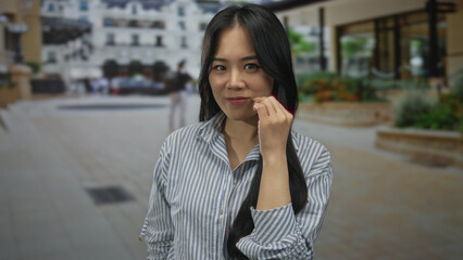 Fototapeta premium Young chinese woman making silence gesture on urban street setting wearing striped shirt outdoors day.