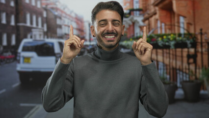 Fototapeta premium Man smiling with eyes closed and pointing finger to object on street with red brick building; optimism.