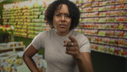 Woman pointing finger and hand on hip by a colorful wall of seed packets on shelves in a building...