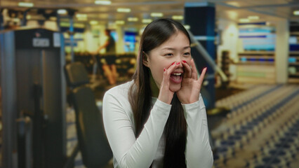 Woman shouting in a gym, with sports equipment blurred in the background, showcasing expressive...