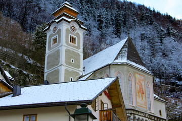 Historic church tower in Hallstatt framed by alpine slopes and snow-capped mountains. A winter...
