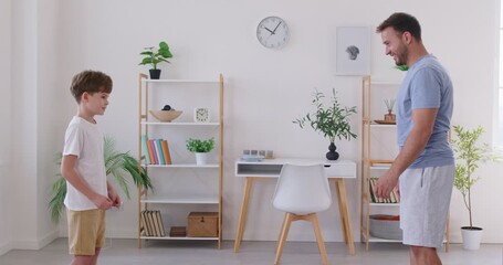 Side view of father and child training martial arts fighting techniques in living room at home. Dad and son greet each other with bow to show respect and honor and then little boy starts attacking - Powered by Adobe