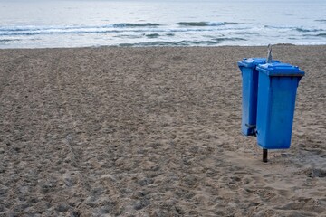 Two blue trash cans standing on sandy beach promoting environmental awareness