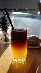 Cool drink with coffee and orange layer in a glass on a wooden table. Perfect for summer menu, cafe or drinks blog.