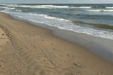 Ocean waves crashing on sandy beach with tire tracks