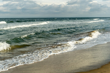 Ocean waves gently crashing on sandy beach under cloudy sky