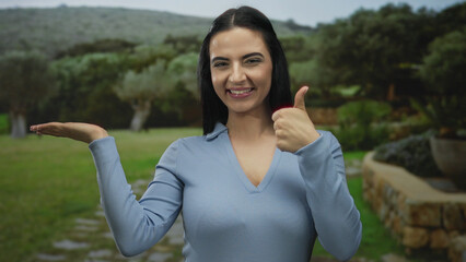 Young hispanic woman in park gestures with thumb up and smiles creating a positive outdoor vibe...