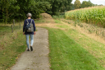 Fototapeta premium Senior woman walking on a countryside path near a cornfield