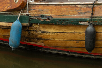 Old wooden boat hull with fenders hanging showing signs of wear and tear