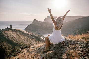 A woman is sitting on a rock overlooking the ocean