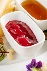 Close-up of a vibrant red berry sauce and golden honey served in elegant white bowls. Fresh herbs, nuts, and greens complete the gourmet breakfast or dessert presentation.