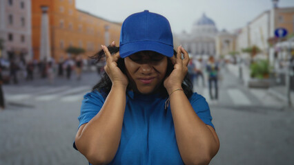 Woman in blue t shirt and cap presses her temples with both hands in san pedro square under...