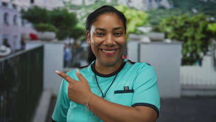 Referee woman in striped jersey holds a silver whistle and points thumb while smiling on a street;...