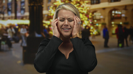 Woman face lifted with closed eyes and open mouth on busy street at night by illuminated tree lights; anxiety.