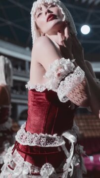 Sensual burlesque dancer in a red and white costume dancing on stage. She is wearing a pearl headpiece.
