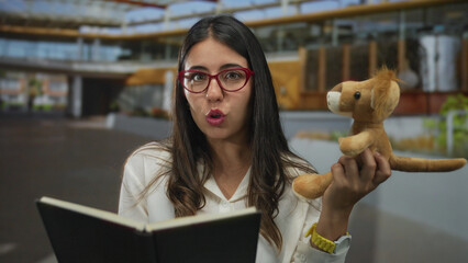 Woman reading aloud holding a lion puppet, outdoors with glasses, showcasing storytelling on a...