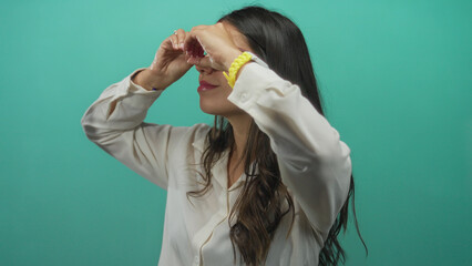 Woman frames her eyes with fingers like binoculars in green studio; discovery exploration curiosity.