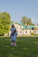 Obraz premium A happy woman and her daughter running through the grass in nature, with a wooden house in the background