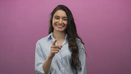Young hispanic woman in blue striped shirt smiling and pointing finger in pink studio; confidence...