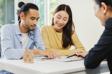 An Asian couple reads the contract before signing the purchase of a new home with a bank officer.